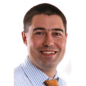 A man wearing a striped shirt and tie is smiling for the camera.