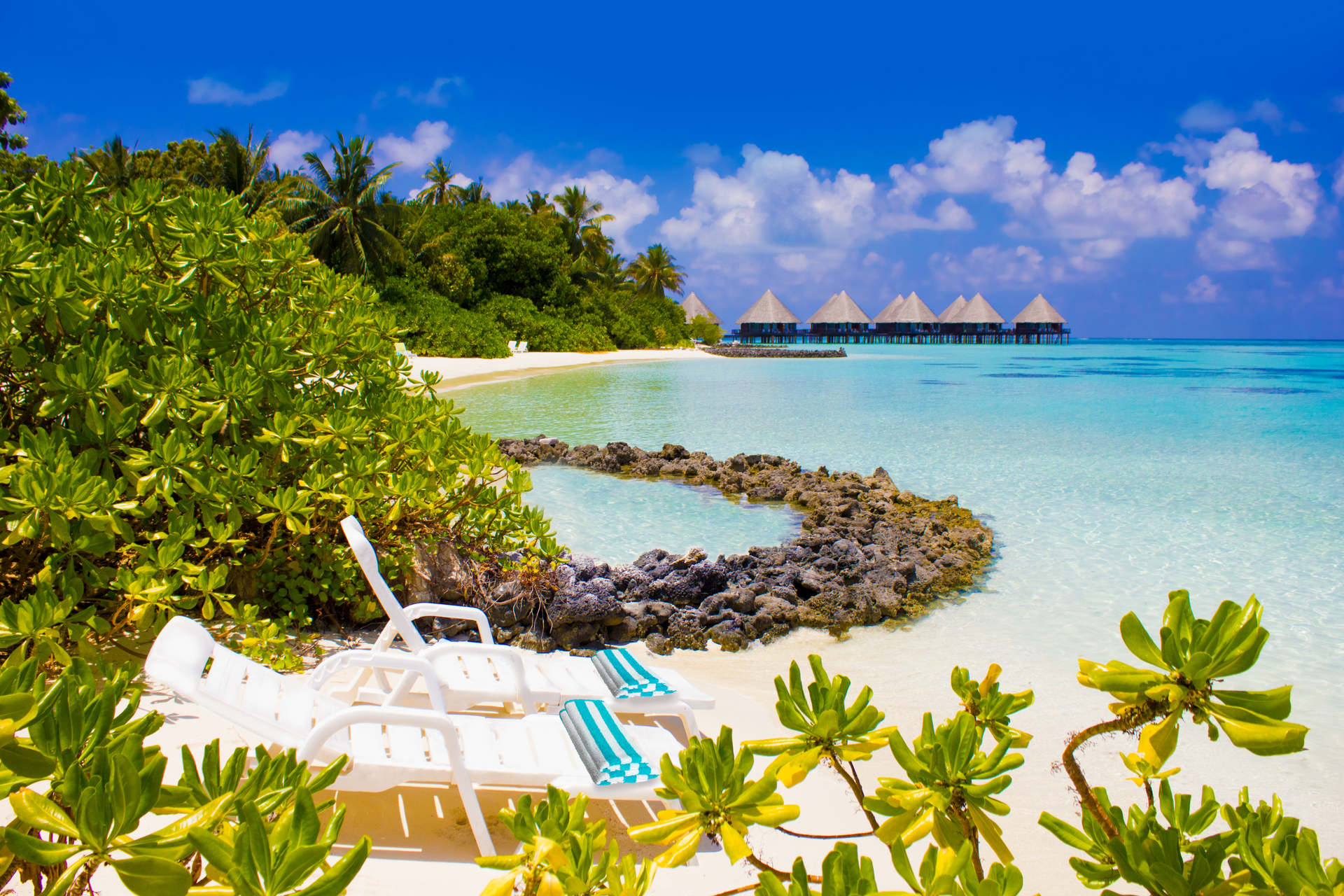 There are two lounge chairs on the beach near the water.