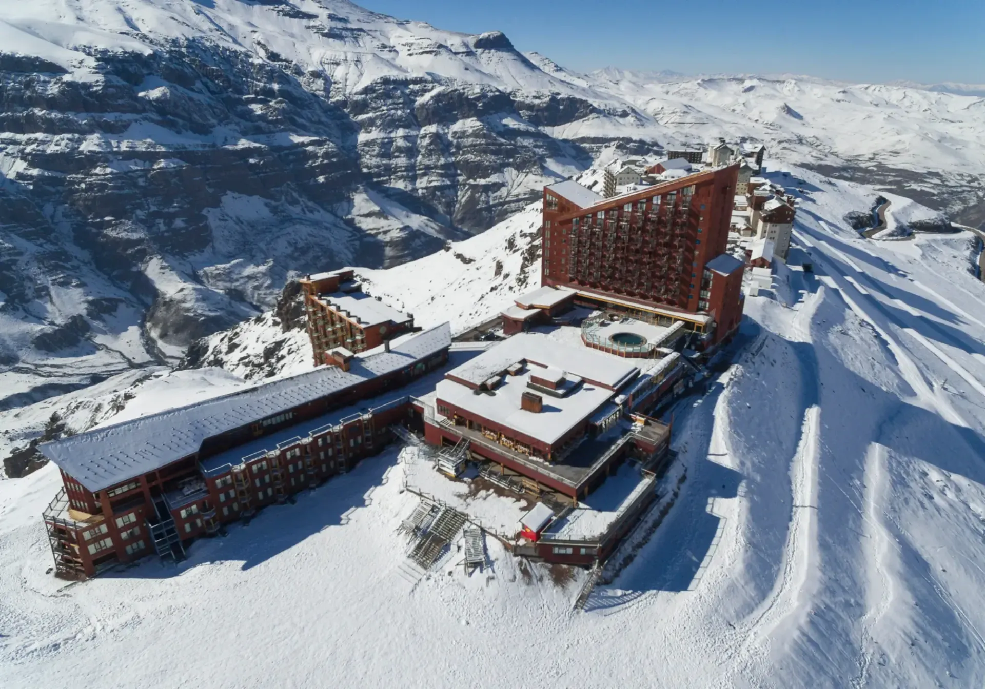 Snow-covered mountain lodge complex with ski slopes and rugged peaks in the background