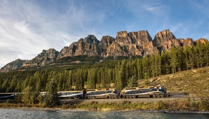A train is going down the tracks in front of a mountain.