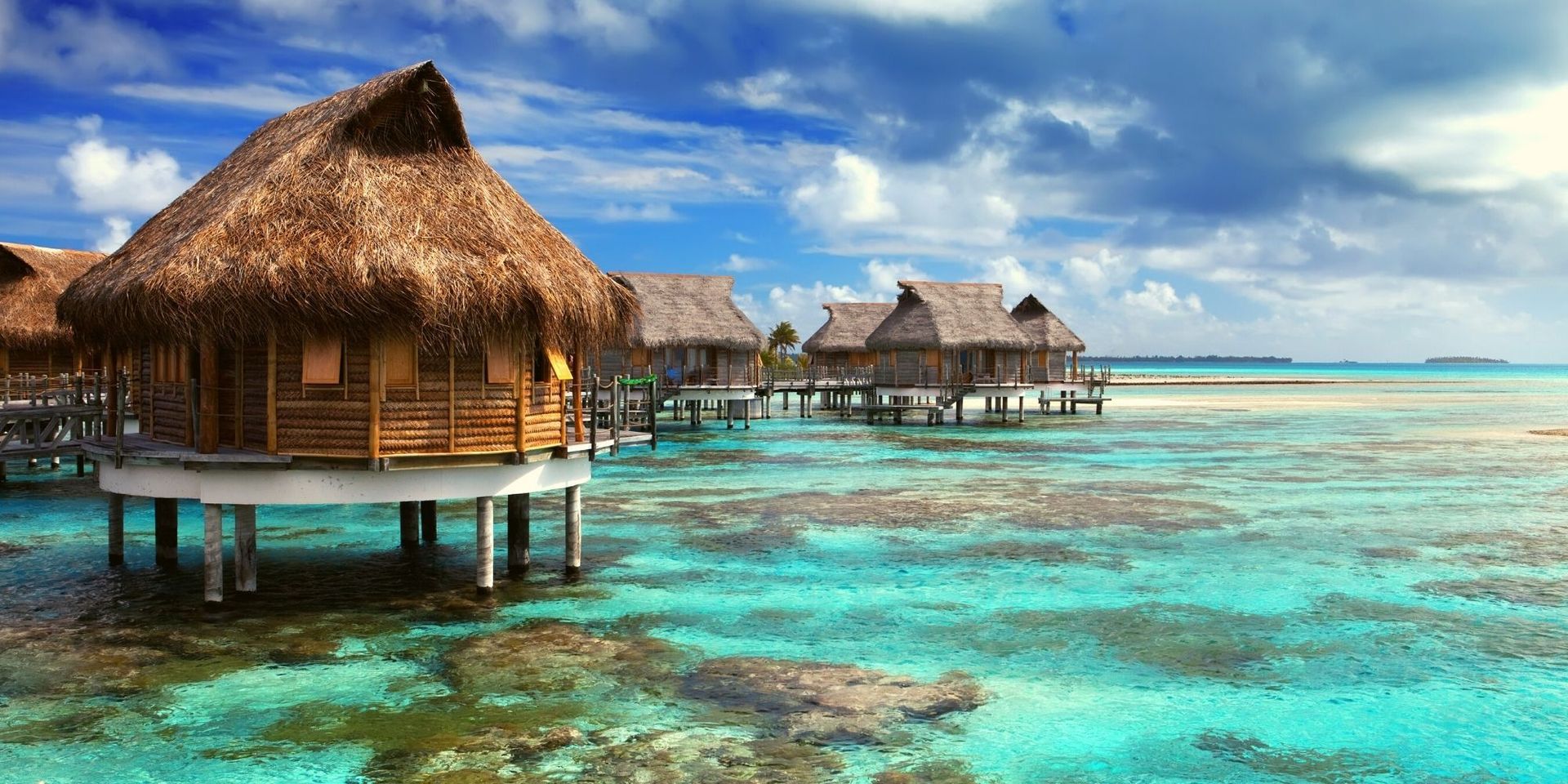 A row of thatched huts in the middle of the ocean.