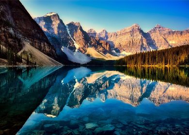 Mountains are reflected in a lake with trees in the foreground