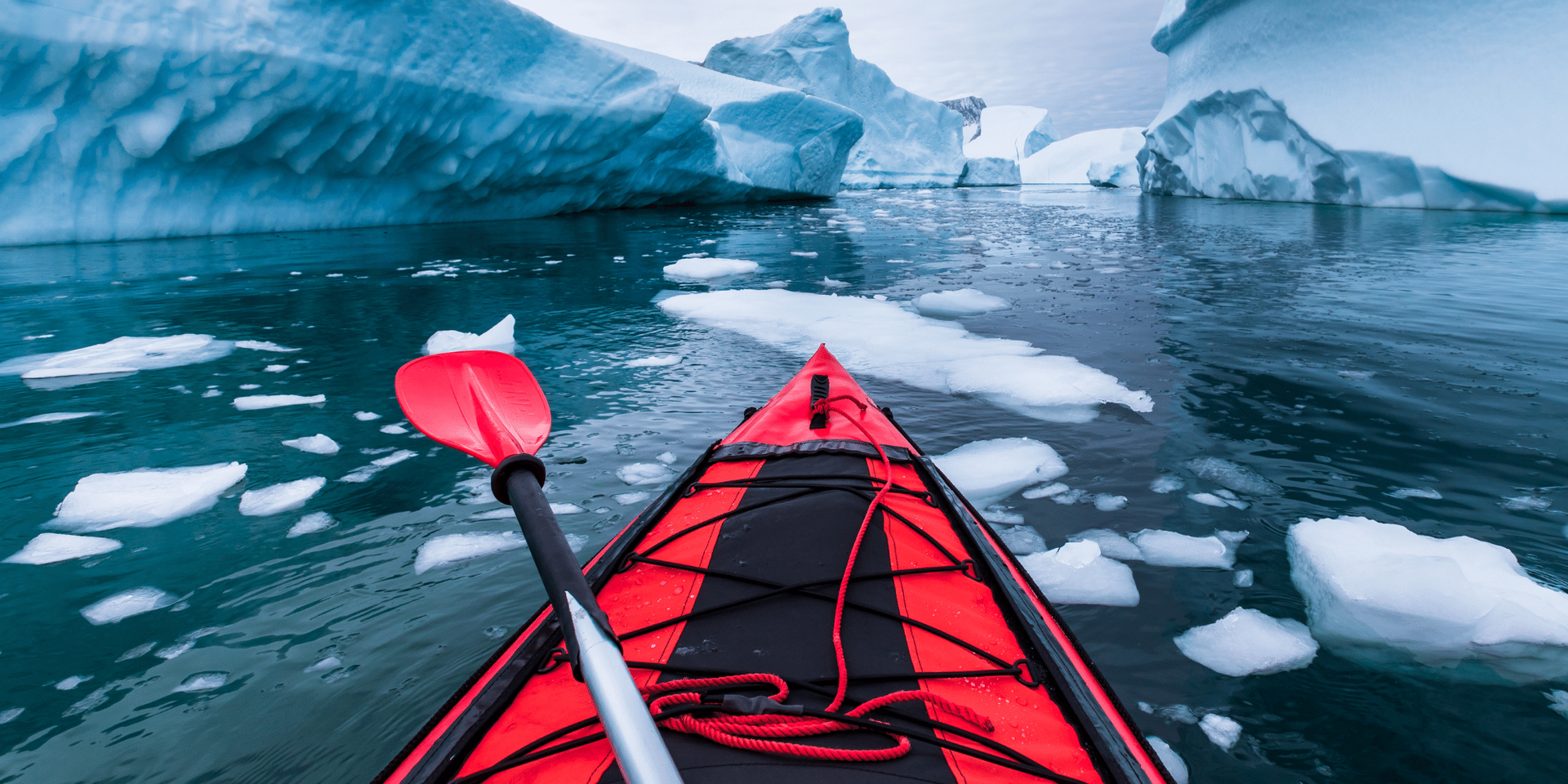 A kayaker is paddling on top of a body of water in antarctica with icebergs in the background.