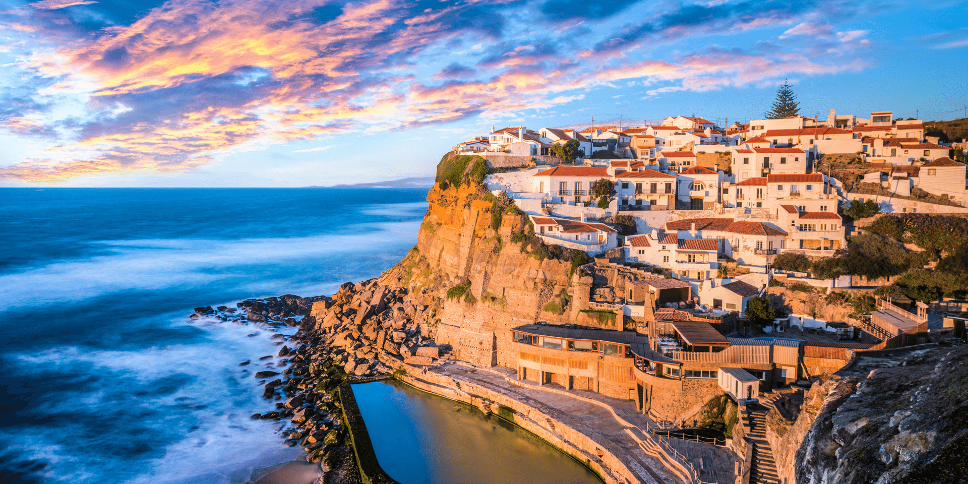 A small town on a cliff overlooking the ocean at sunset.