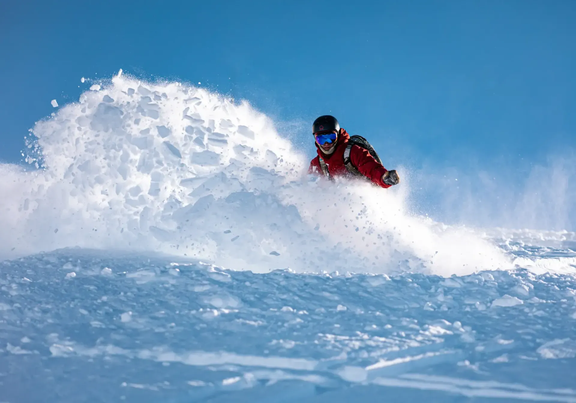 Snowboarder in red jacket carving through powder on a bright blue slope