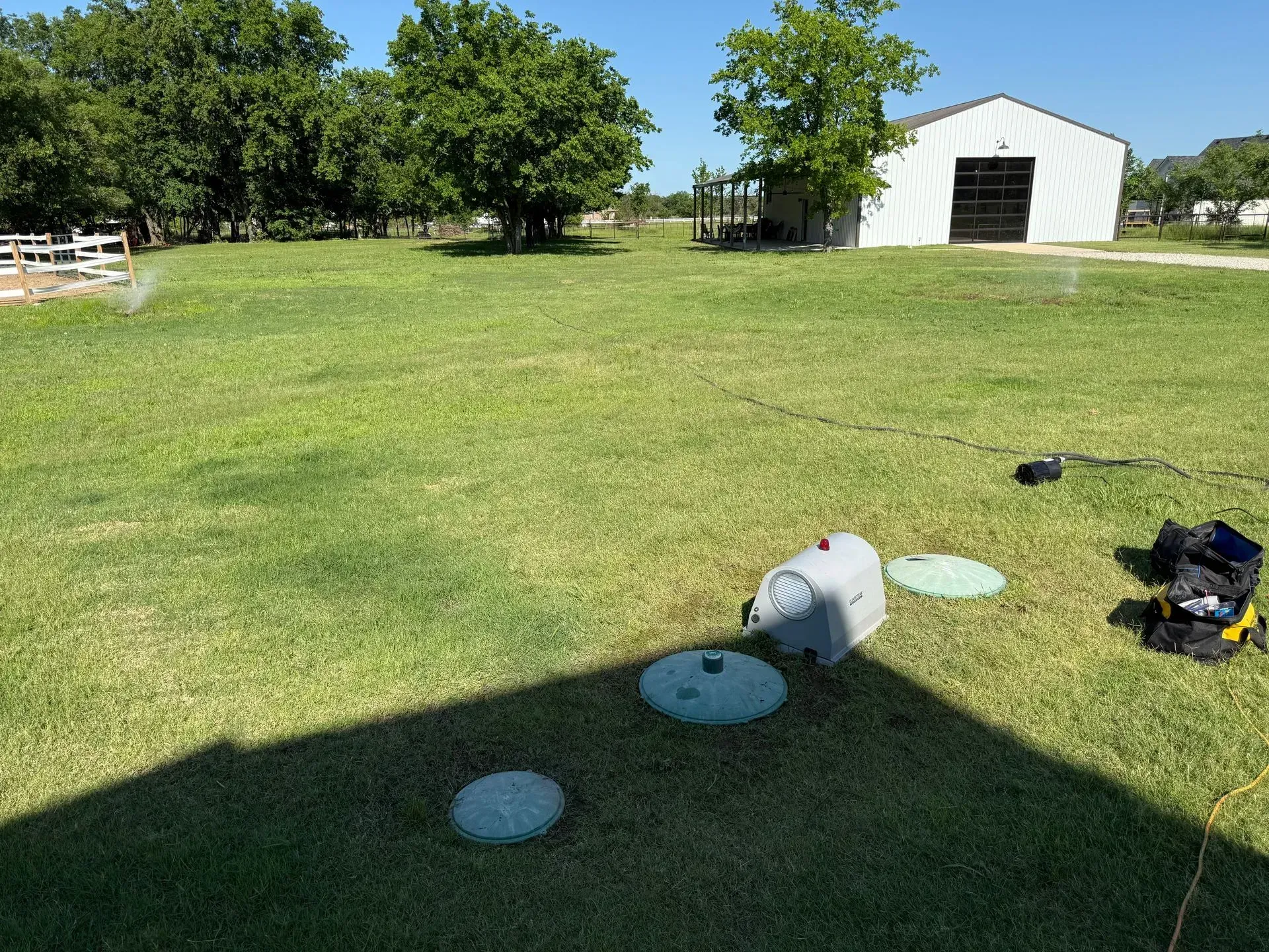 Green lawn with septic system access points; white building in the background. Sunny day.