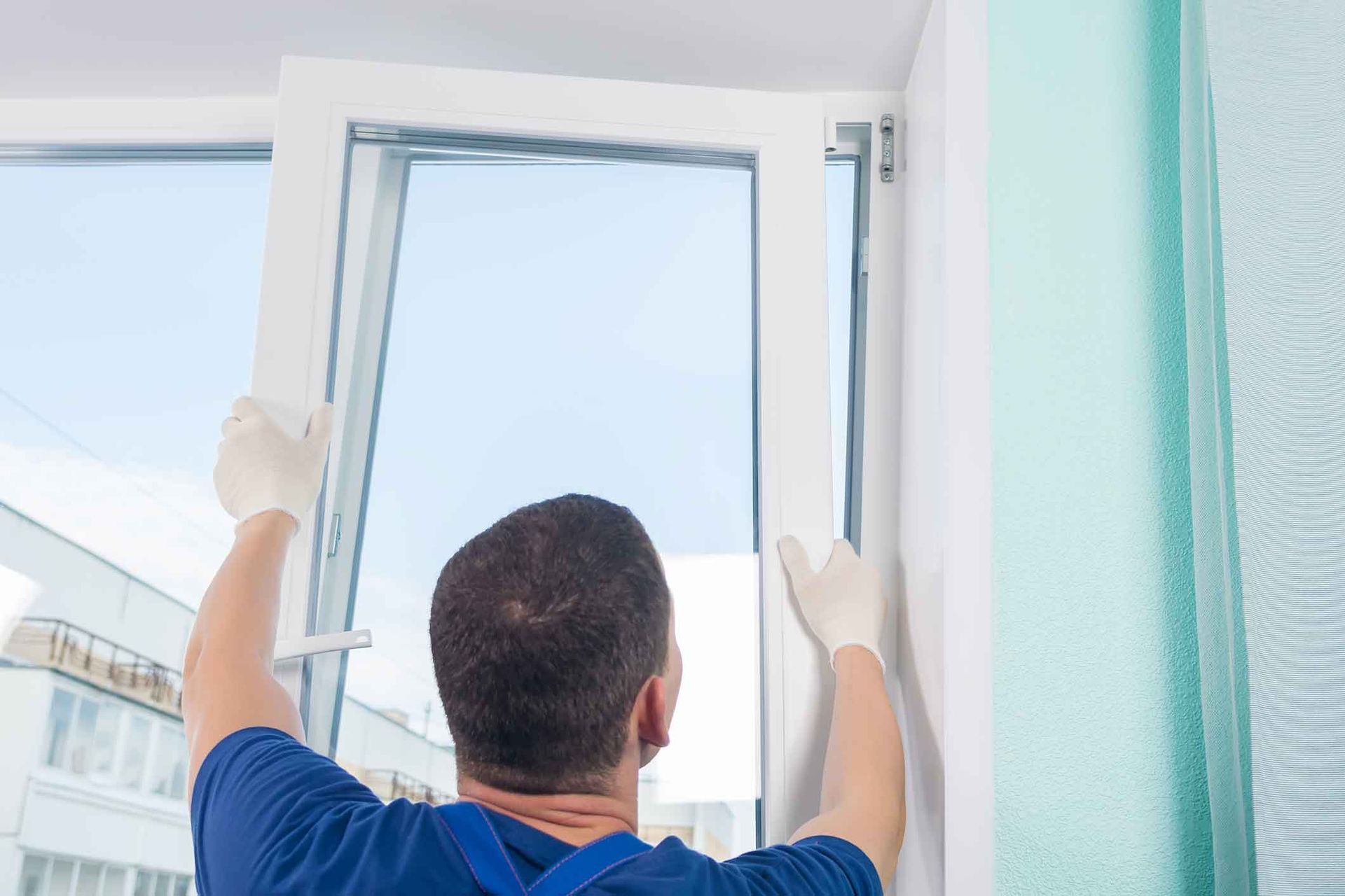 Person wearing gloves installing a white window in a room.