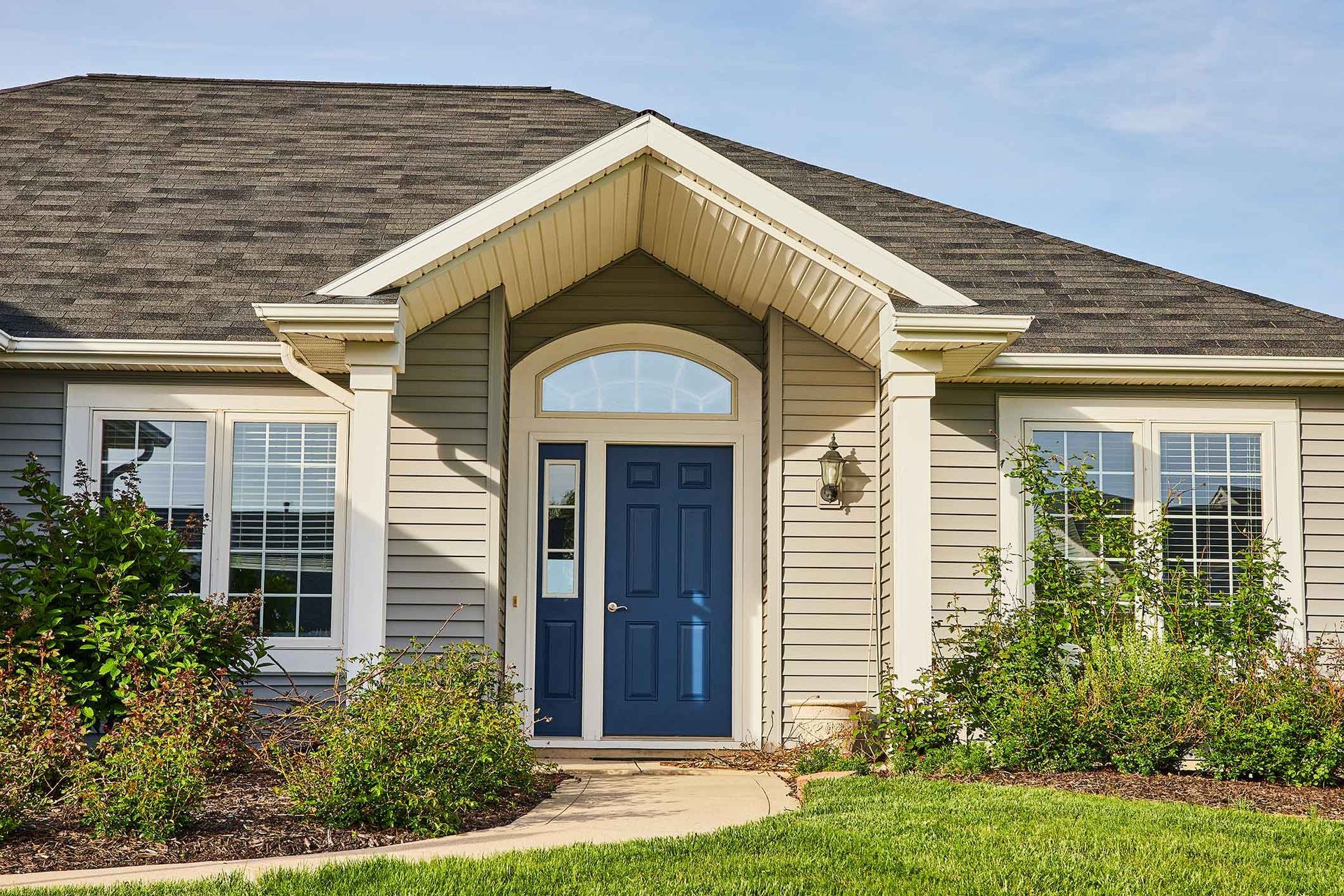 Blue front door on a gray house with windows and a path, under a light brown portico.