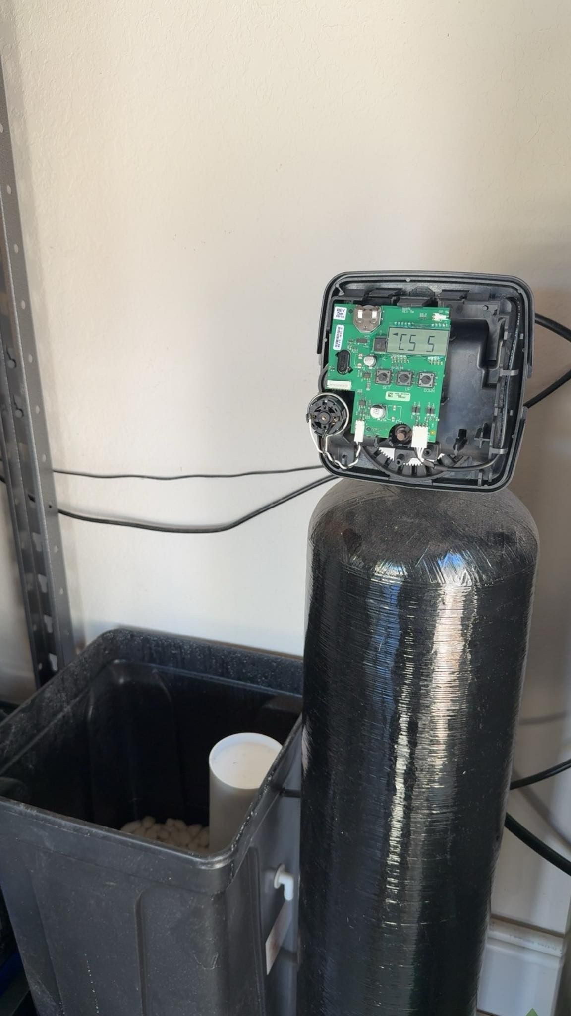 Water softener with exposed electronic control panel. A salt bin is in the foreground.