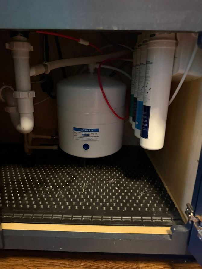 Under-sink water filter system with tank and multiple filter cartridges, installed within a blue cabinet.