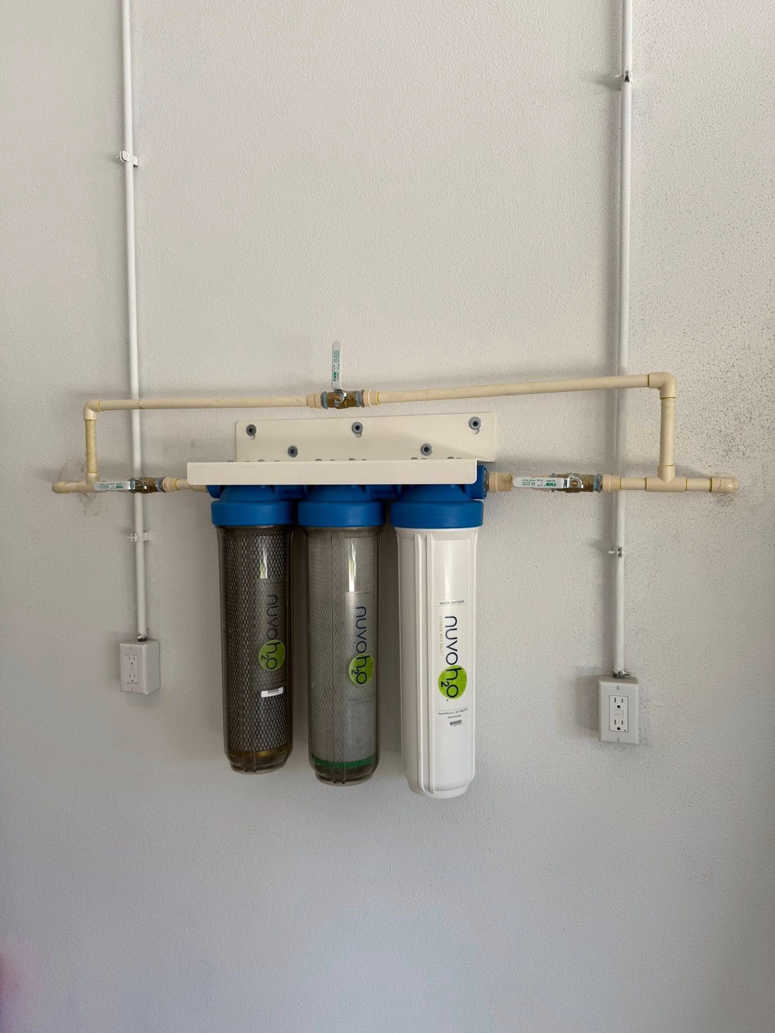 Three water filters mounted on a white wall, connected by beige pipes.