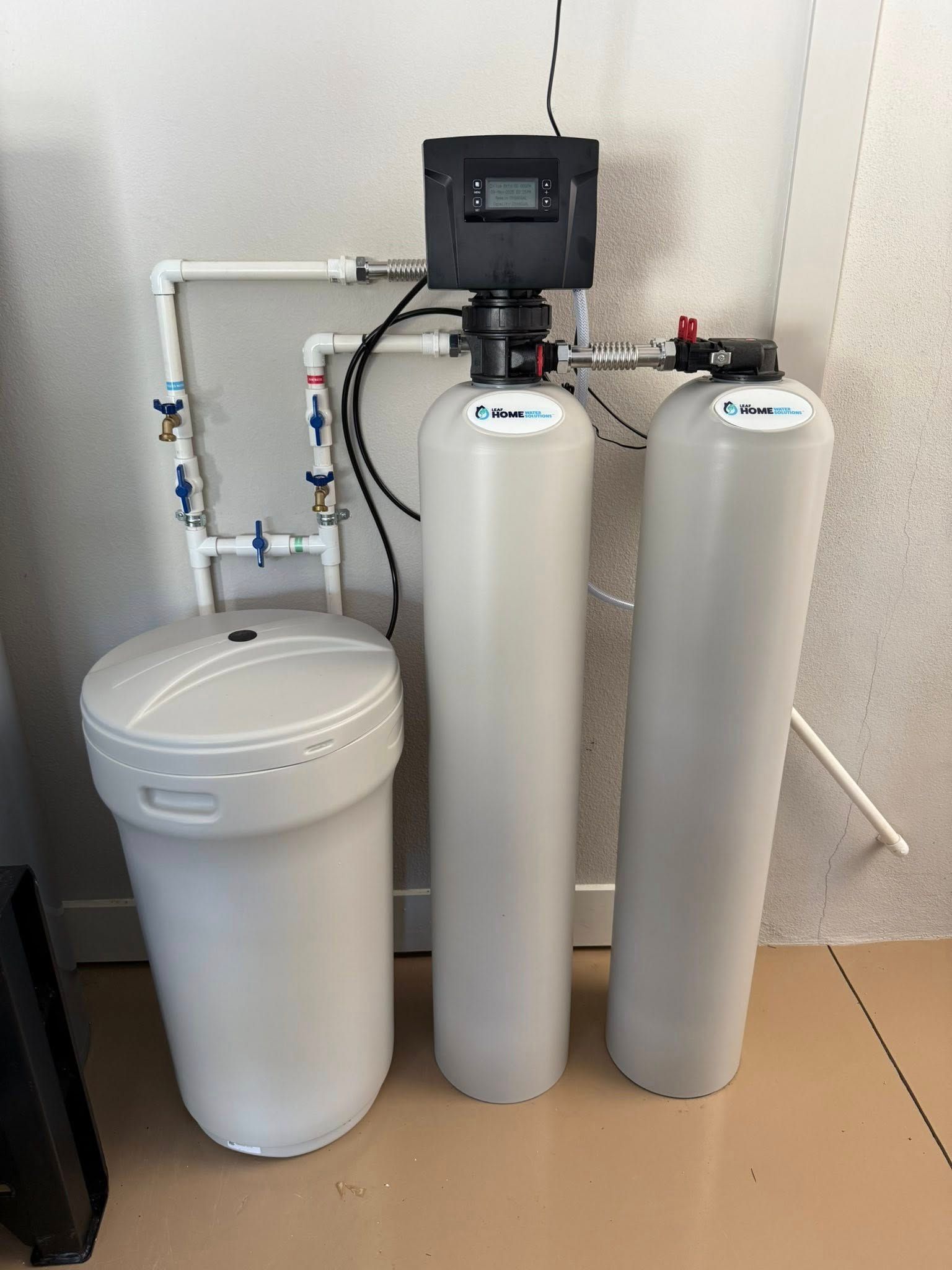 Water filtration system with three cylindrical tanks and a salt storage unit, set against a wall.