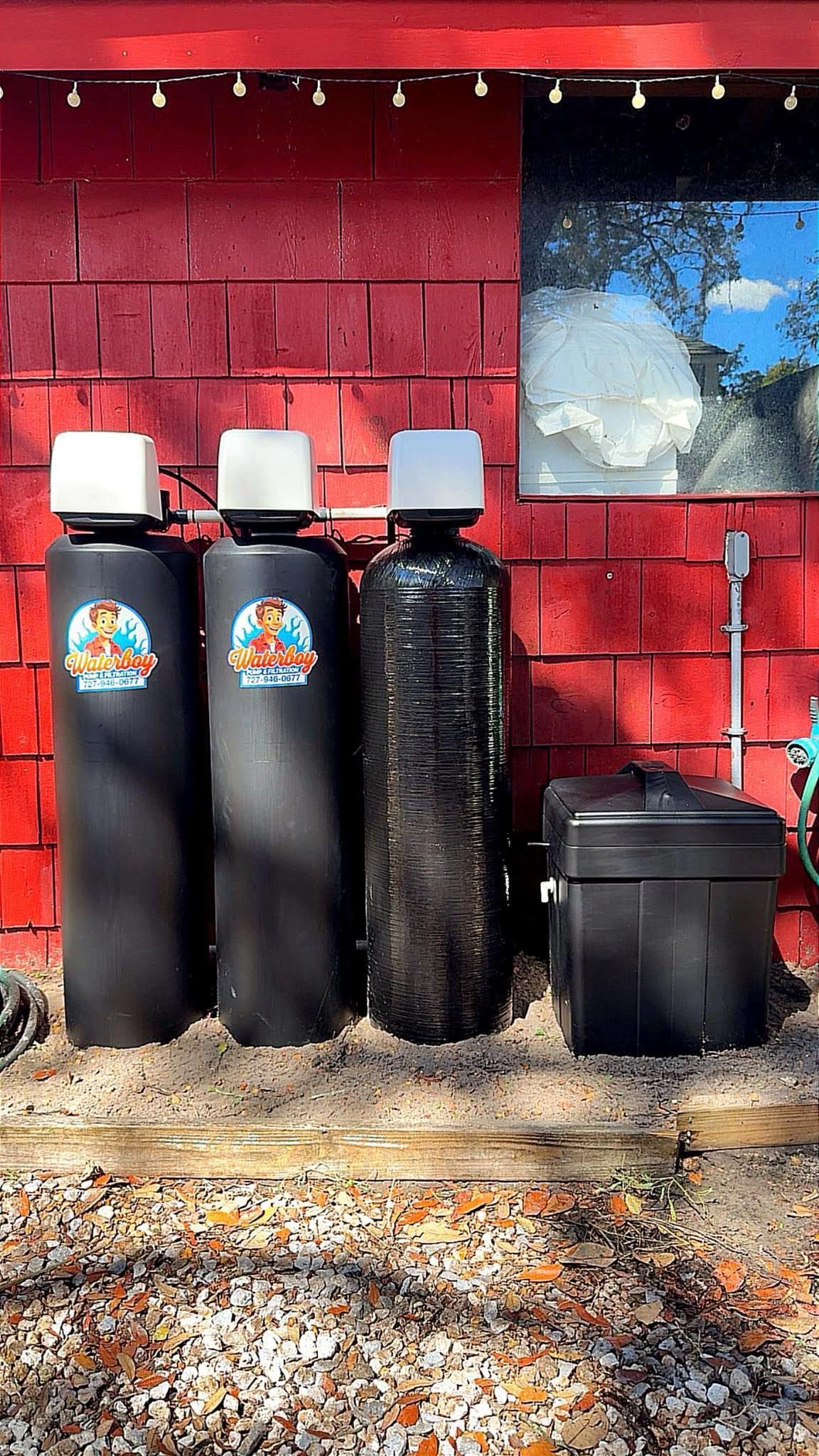 Three black water tanks with white tops against a red brick wall, next to a black box.