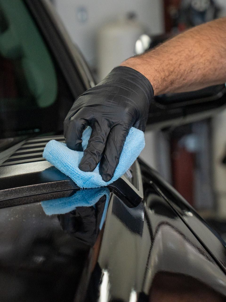 A person is using a blue squeegee to remove plastic from the hood of a car