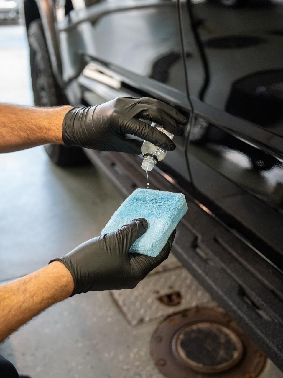 A person wearing black gloves is polishing a black car