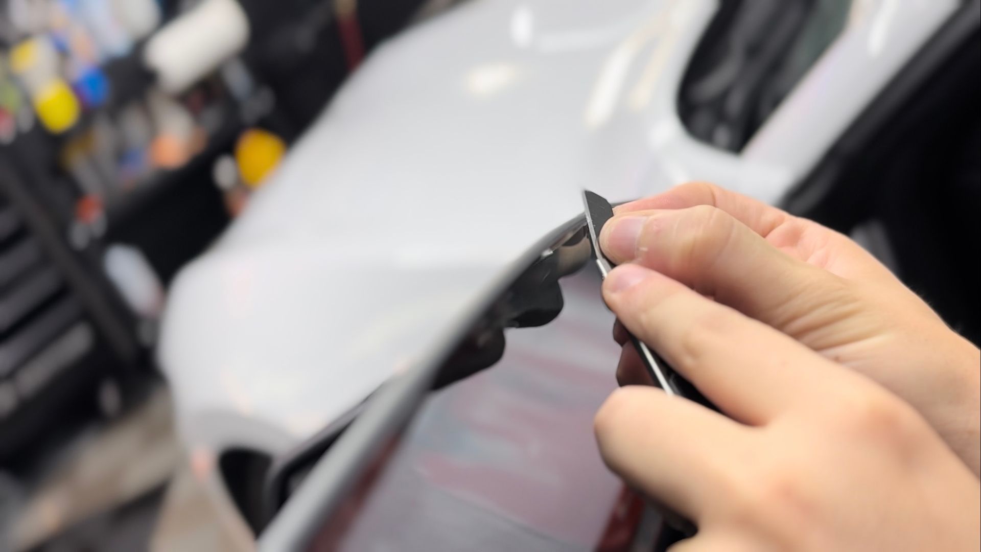 A person is holding a piece of metal in front of a white car.