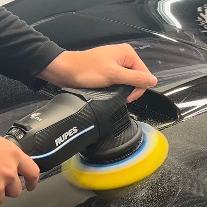 A person is polishing a black car with a rupes machine