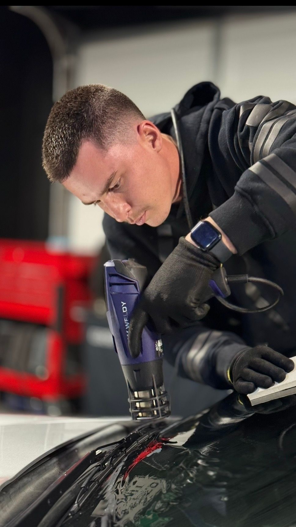 A person is using a blue squeegee to remove plastic from the hood of a car