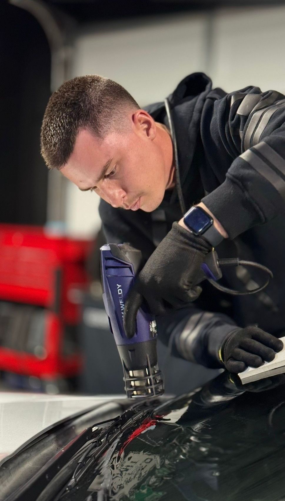 A man is working on tinting a car windshield with a tool.