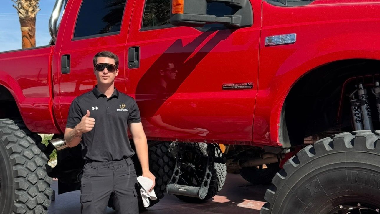 A man is standing in front of a red truck giving a thumbs up.