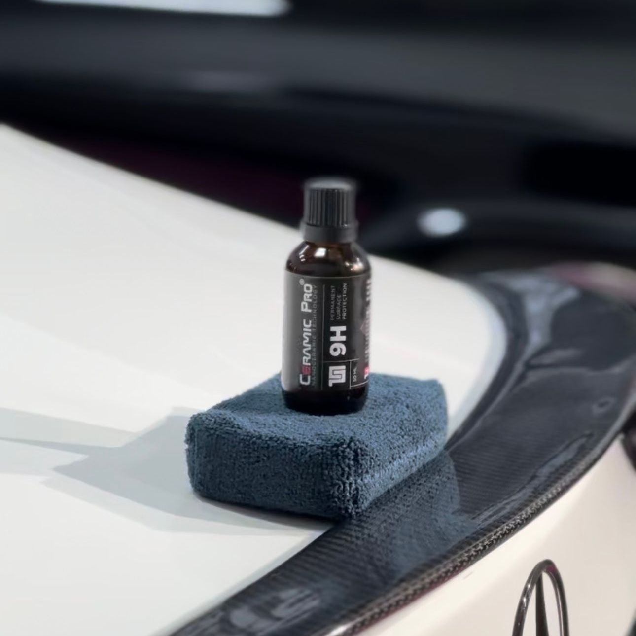A bottle of ceramic pro is sitting on a blue towel on the hood of a car.