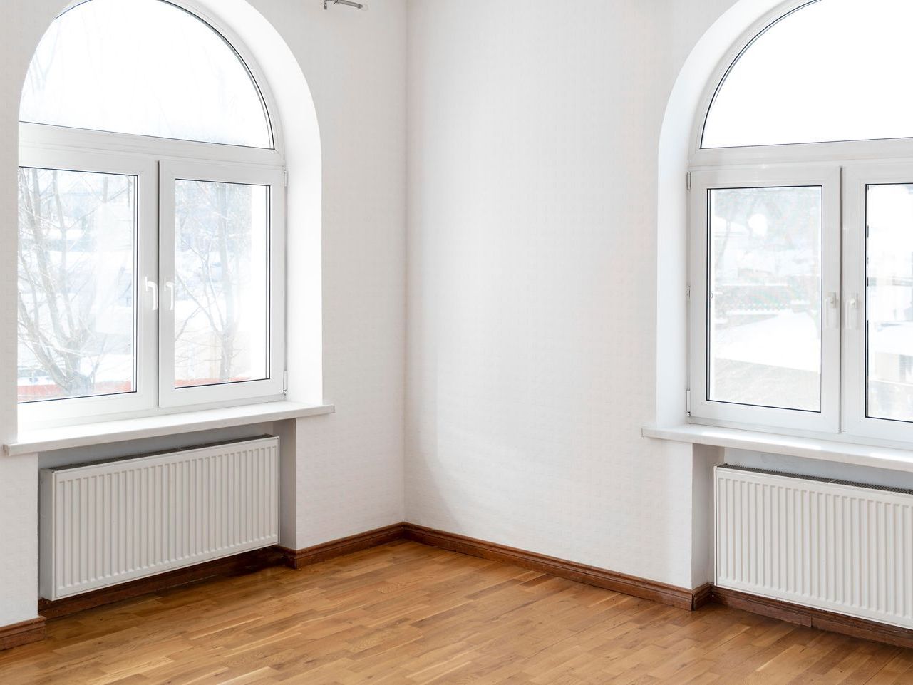 An empty room with arched windows and hardwood floors