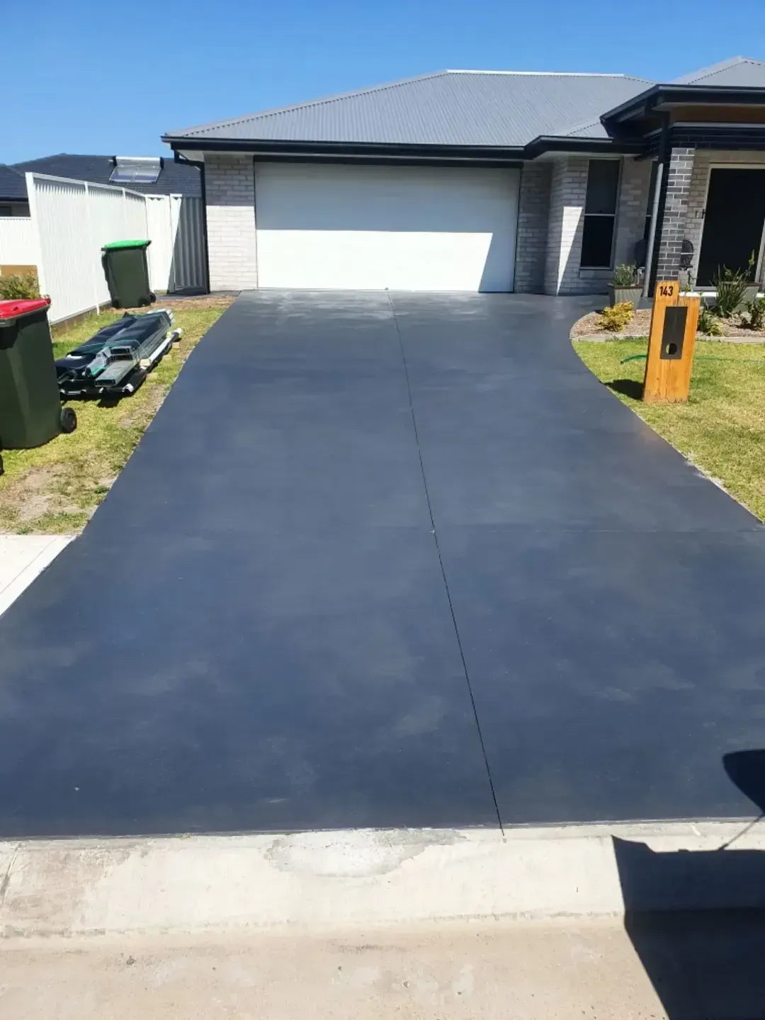 A Concrete Driveway Leading To A House With Trash Cans On The Side Of It — DCK Concreting In Laurieton, NSW