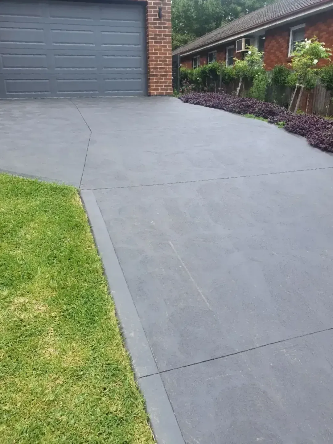 A Driveway Leading To A Garage With A Brick House In The Background — DCK Concreting In Lake Cathie, NSW