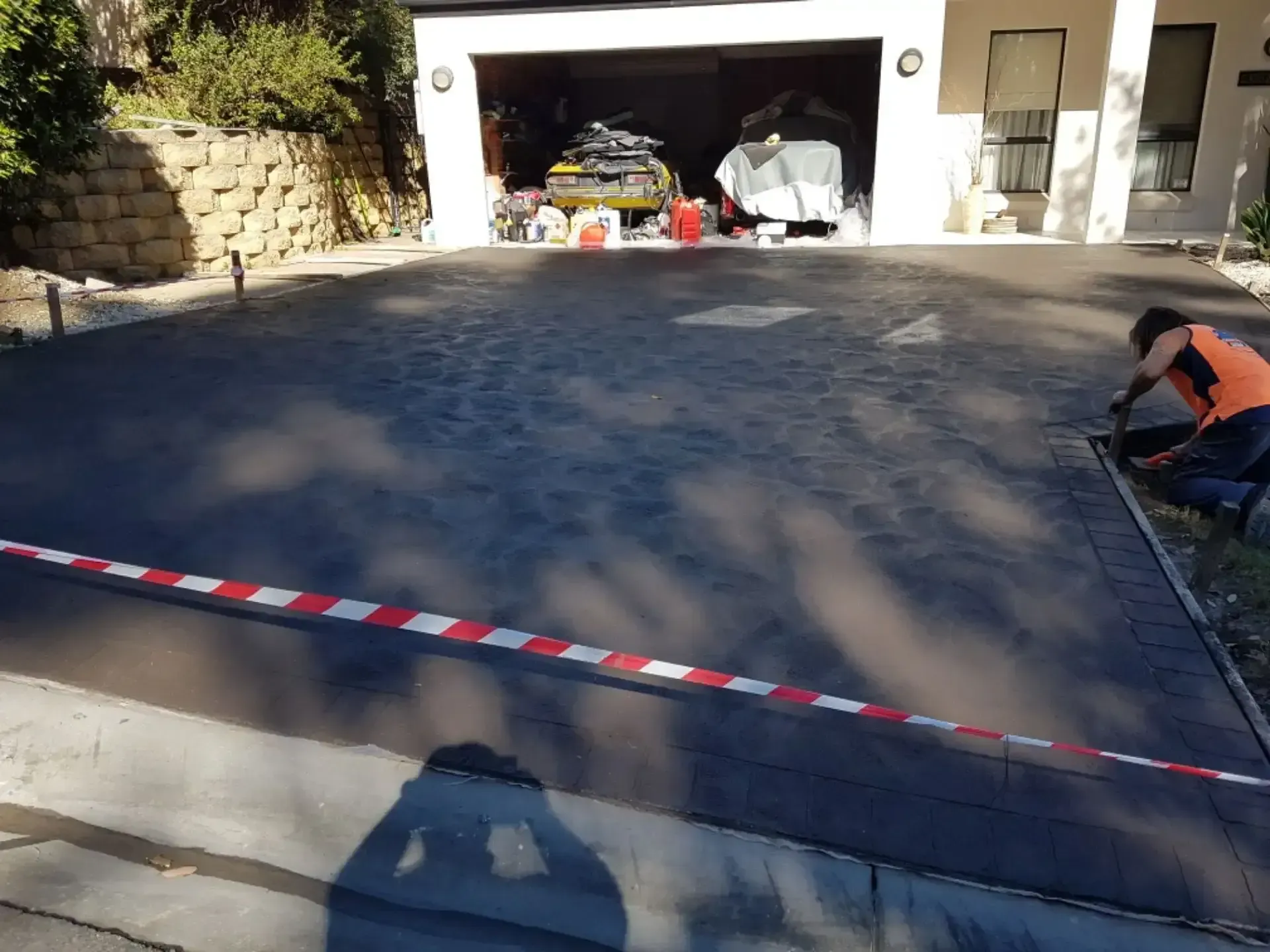 A Man Is Working On A Driveway In Front Of A Garage — DCK Concreting In Lake Cathie, NSW