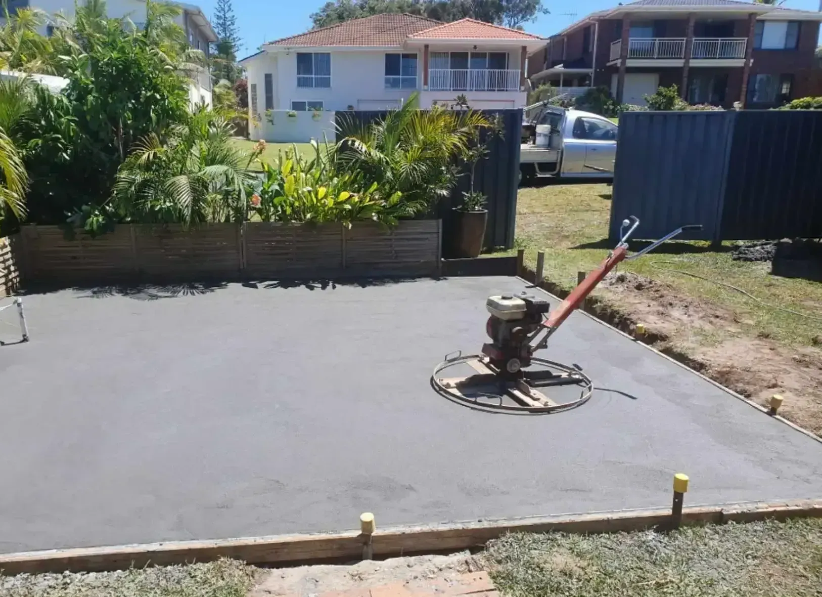 A Machine Is Laying Concrete In A Yard In Front Of A House — DCK Concreting In Lake Cathie, NSW