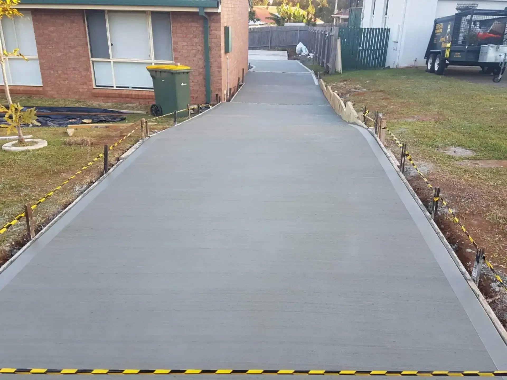 A Concrete Driveway Is Being Built In Front Of A Brick House — DCK Concreting In Lake Cathie, NSW