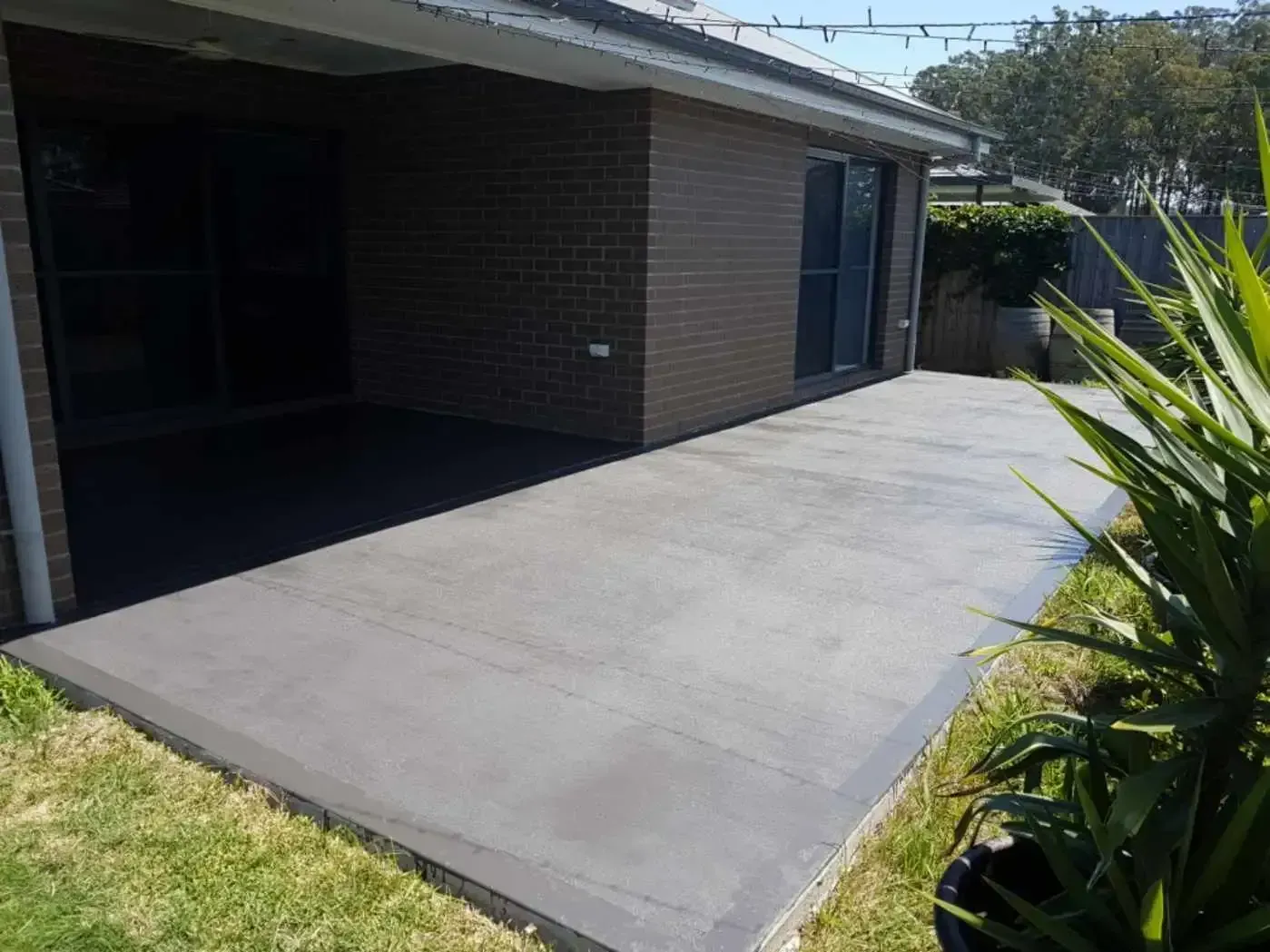 A Brick House With A Concrete Patio In Front Of It — DCK Concreting In Lake Cathie, NSW