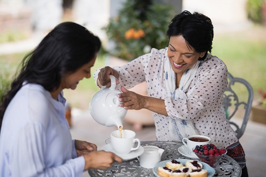 A smiling woman pouring tea in a cup for hear daughter while they talk. With new dental implants, she's extending the amount of time she has to smile.
