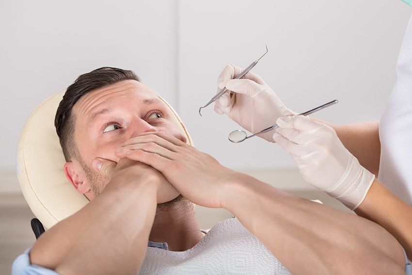 A Frightened Man At Dentist Office Covered Mouth With Hands. While you might be scared of the dentist, at Riverlands Dental we can offer you sedation therapy so that you can have the smile you deserve.