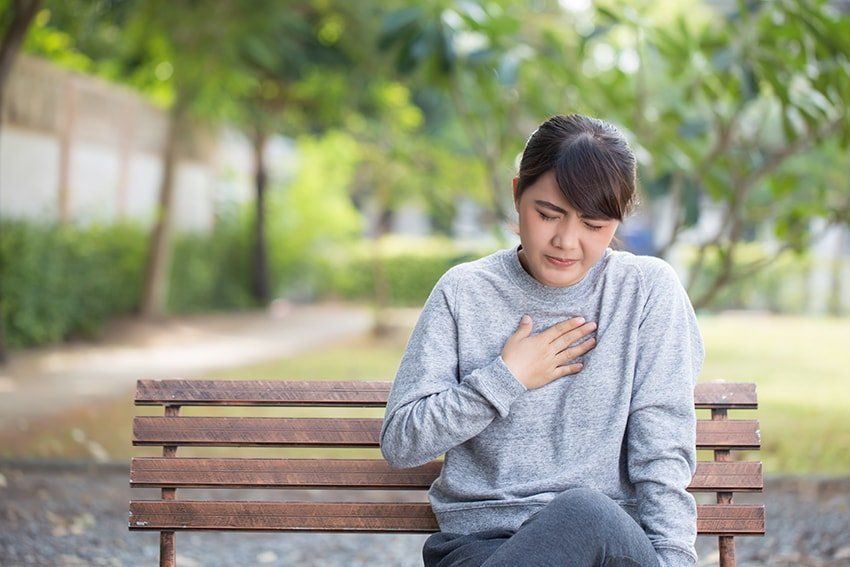 Young asian woman suffering from acid reflux, holding her chest while it burns. Reflux Can Cause Serious Tooth Damage