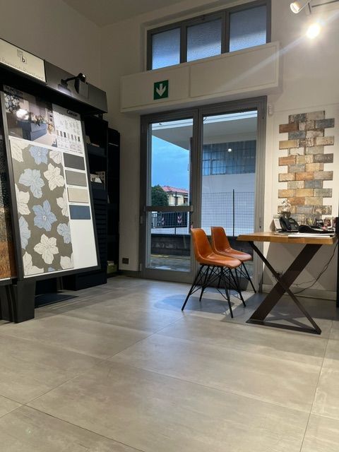 Interno dello showroom di piastrelle, con esposizione di campioni di piastrelle, tavolo, sedie e ampia finestra.