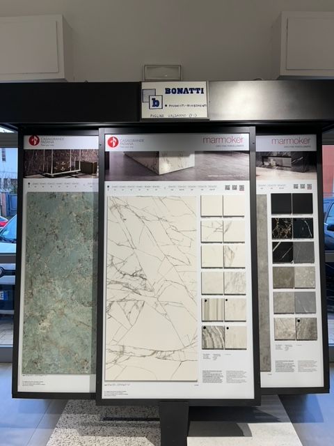 Esposizione di piastrelle con tre pannelli incorniciati che mostrano vari motivi e texture di pietra.