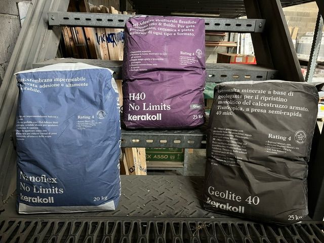 Tre sacchi di materiale da costruzione del marchio Korakoll nei colori blu, viola e nero su scale di metallo.