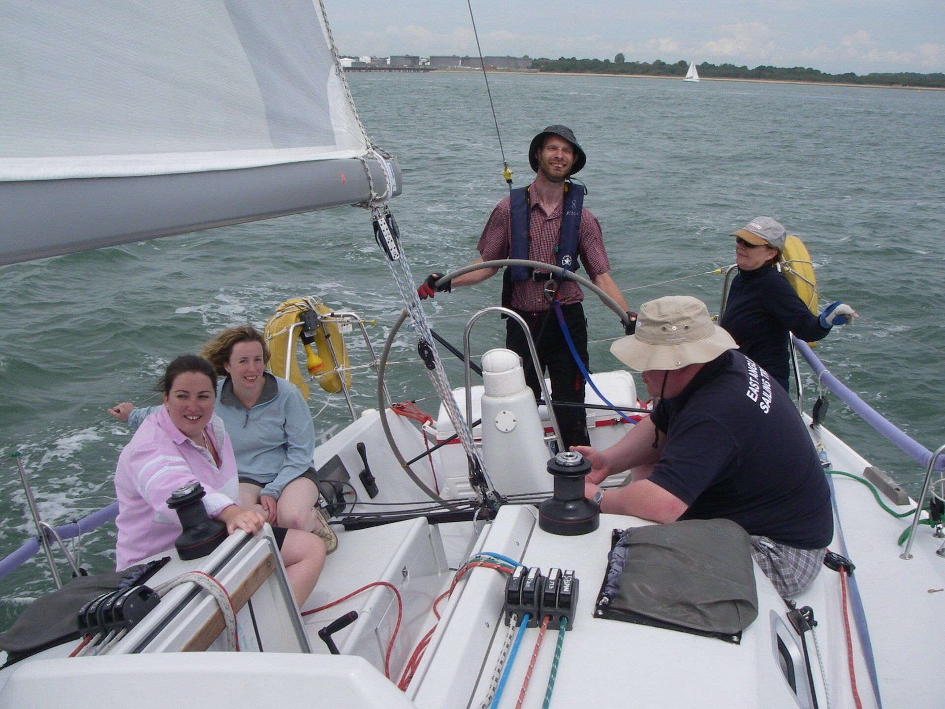 A picture of a V.I. sailor at the helm of an underway yacht. The rest of the mixed crew are sitting nearby.