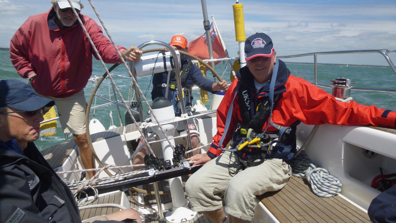 A picture of four V.I. and sighted crew on an underway yacht, which is tilted over under full sail. A V.I.sailor is at the helm, and the other crew are standing and sitting nearby.