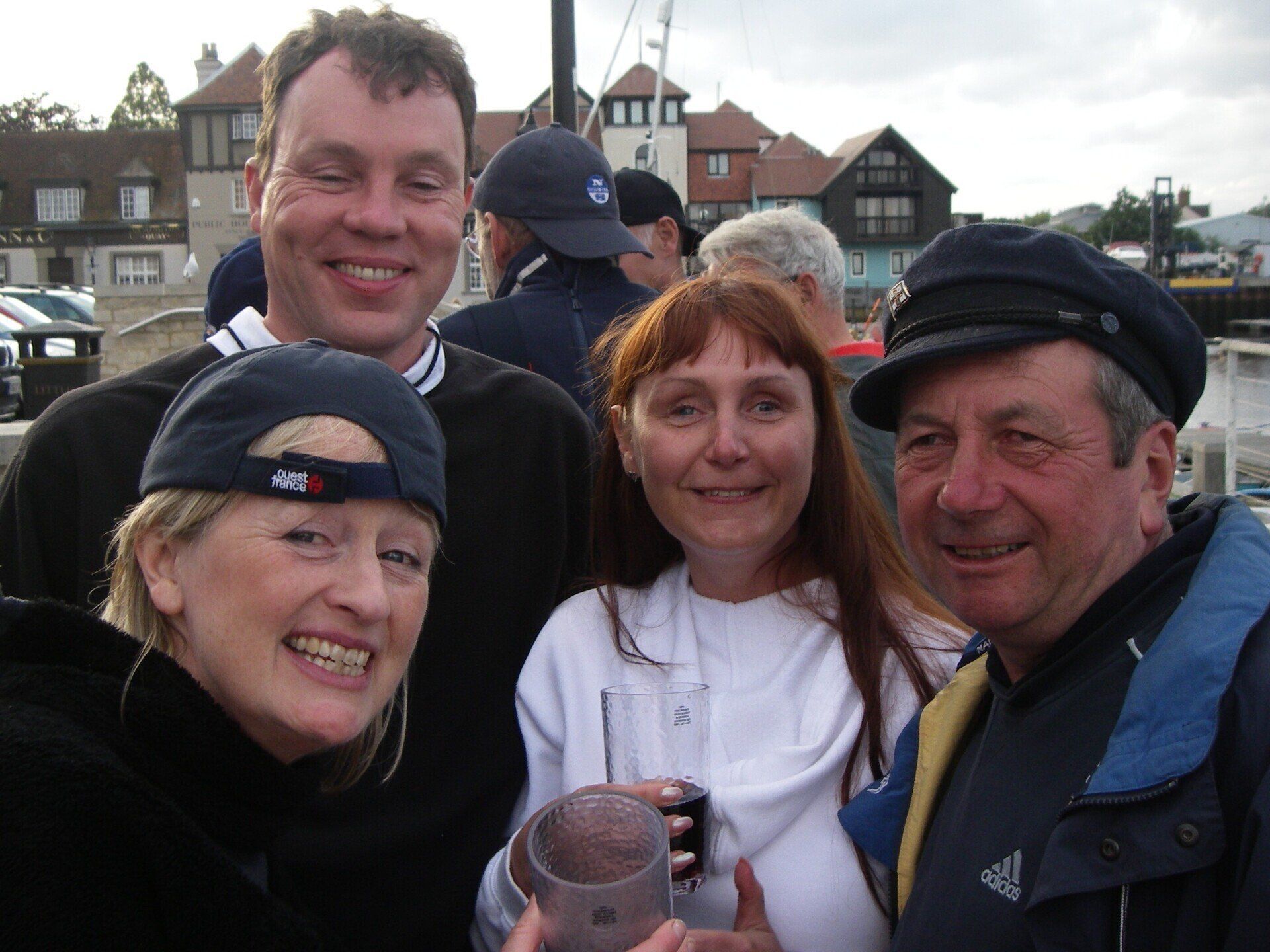 A selfie picture of a group of sighted and V.I. crew taken on the quayside after a day's sailing. They are all smiling at the camera, and a couple are raising glasses.