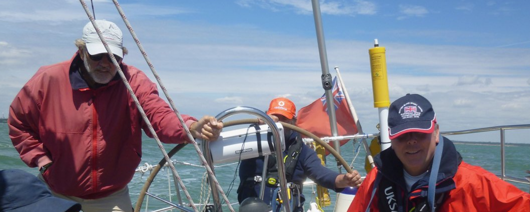 A picture of a sailing yacht underway, taken from the deck looking towards the stern. It is crewed by a mixture of sighted and VI sailors, smiling happily