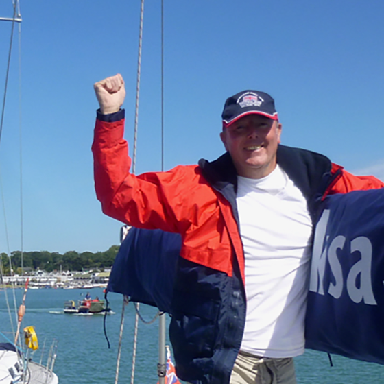 Picture of a male VI sailor smiling and raising his fist in celebration, holding on to a yacht spar.