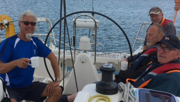 Four sighted and V.I. crew are sitting around the wheel of a yacht having a cup of tea. The helm is currently unmanned and the yacht is stationary.