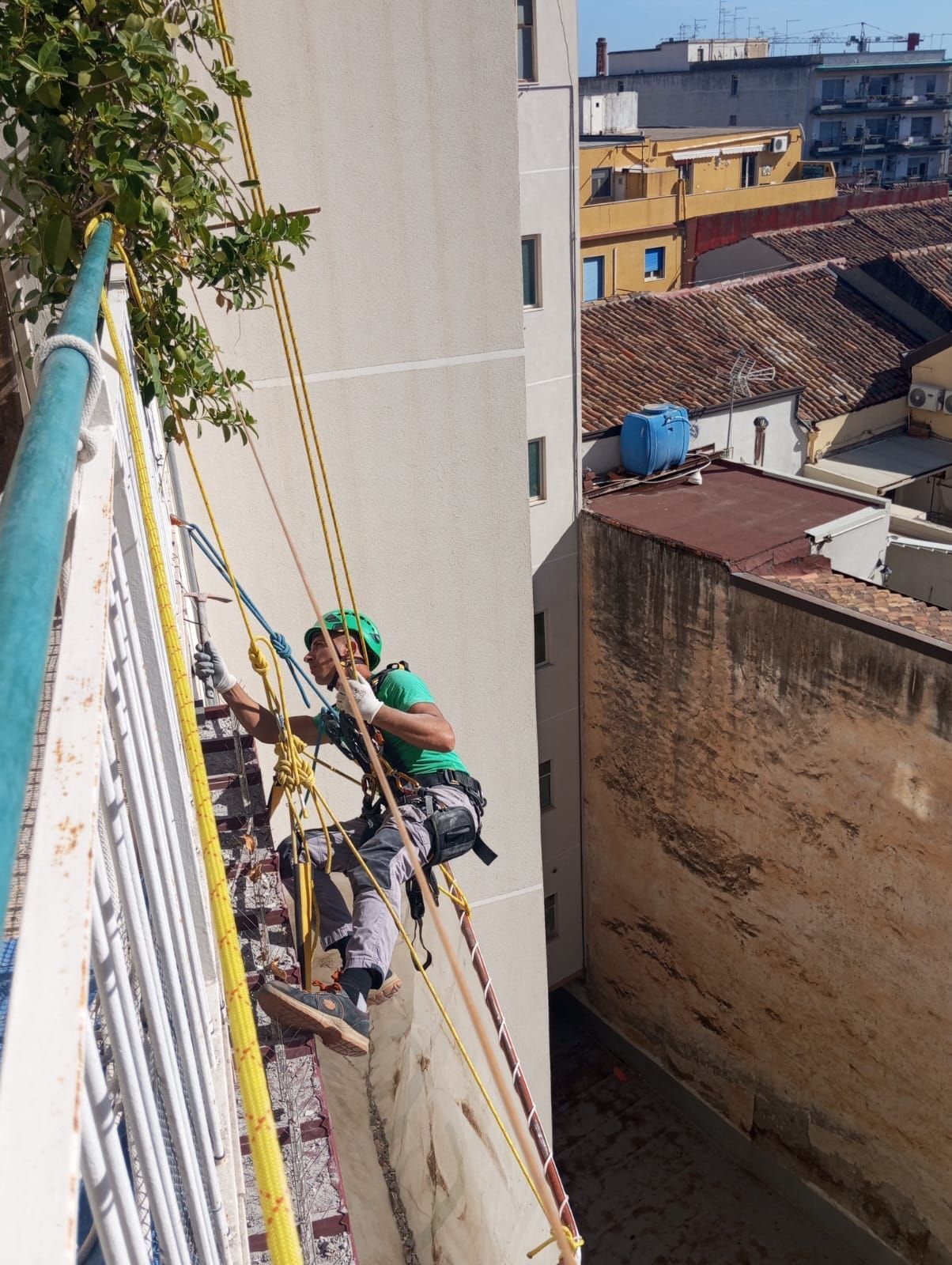 Uomo che si cala in corda doppia da un edificio, fissando le corde, con sullo sfondo il paesaggio urbano.