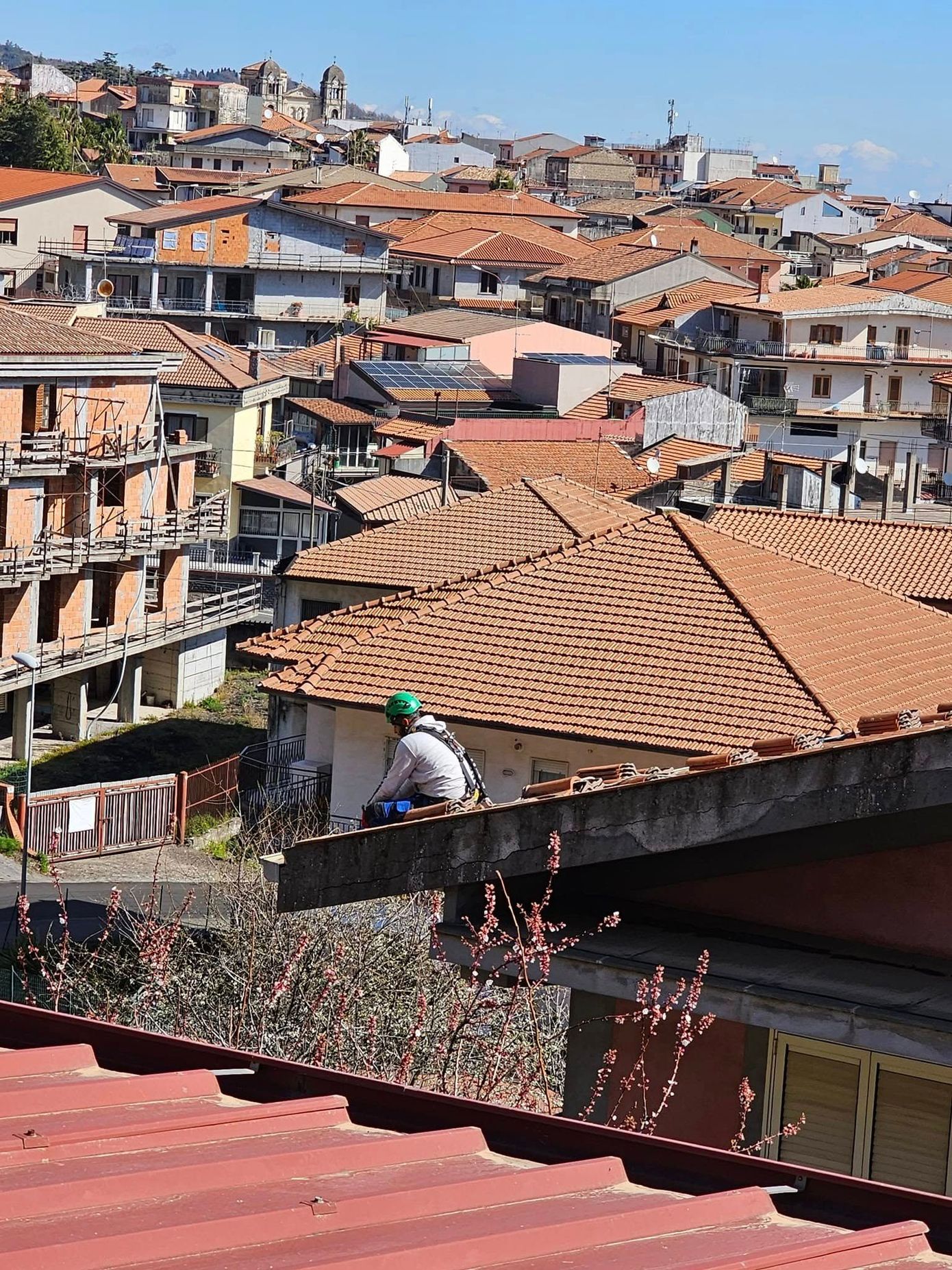 Uomo sul tetto che domina una cittadina collinare con tetti in terracotta.