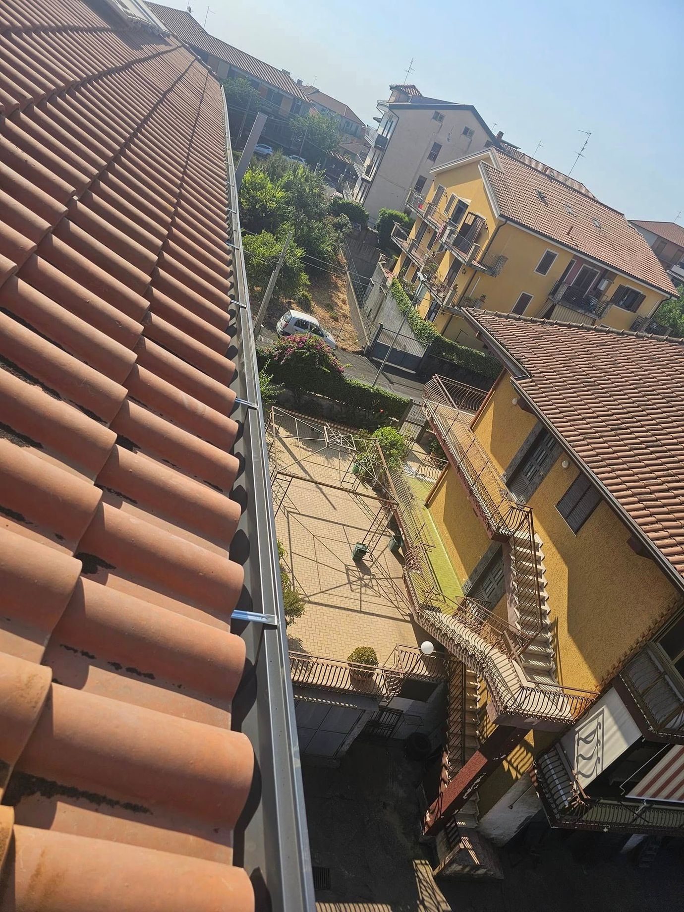 Vista dall'alto di tetti in tegole di terracotta, edifici gialli e una strada con tanto di verde in mezzo. Soleggiato, di giorno.