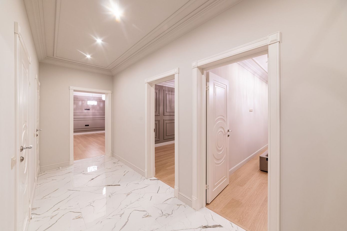Corridoio bianco con pavimento in marmo, porte aperte che conducono alle stanze e illuminazione da incasso.