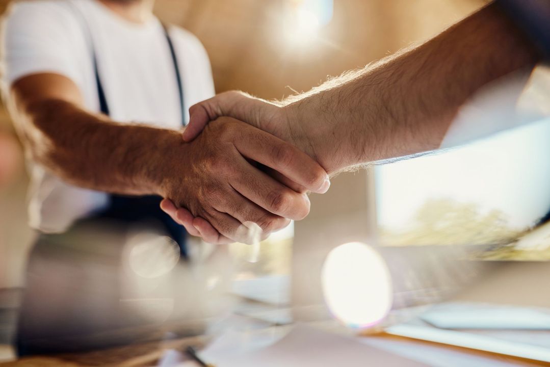 Due persone si stringono la mano, illuminate dalla luce del sole, in un ambiente di lavoro.