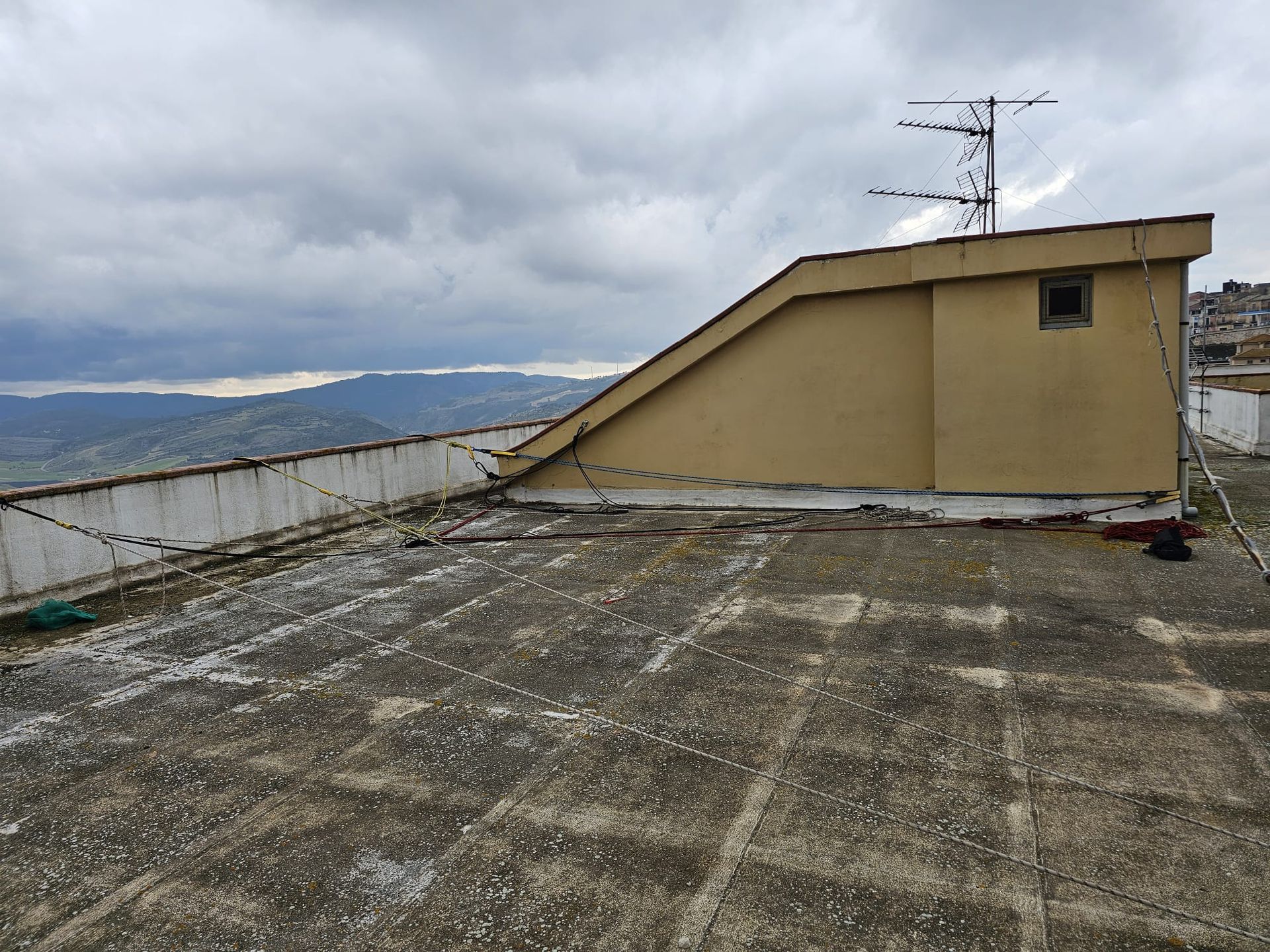 Tetto con antenna, parete inclinata e paesaggio in lontananza sotto un cielo nuvoloso.